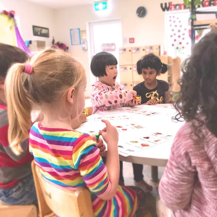 Five children sitting around a low table together, working on a picture card activity with a teacher’s materials spread out in front of them.